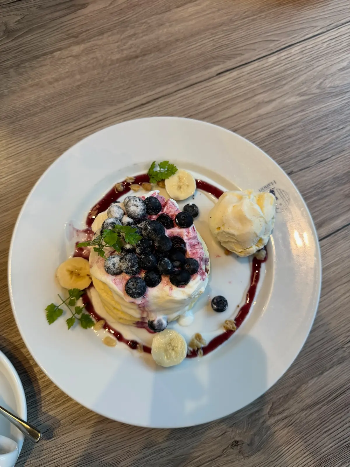 A plate of blueberry pancakes with cream, banana slices, and ice cream.