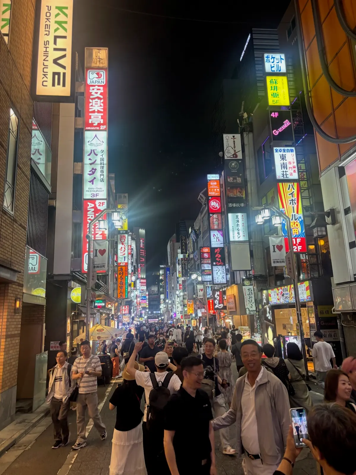 Busy Shinjuku street at night with bright signs.